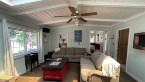 Ein Wohnzimmer mit hoher Decke, einem Deckenventilator, einem Ecksofa, einem roten Couchtisch und einem Fenster mit Vorhängen.