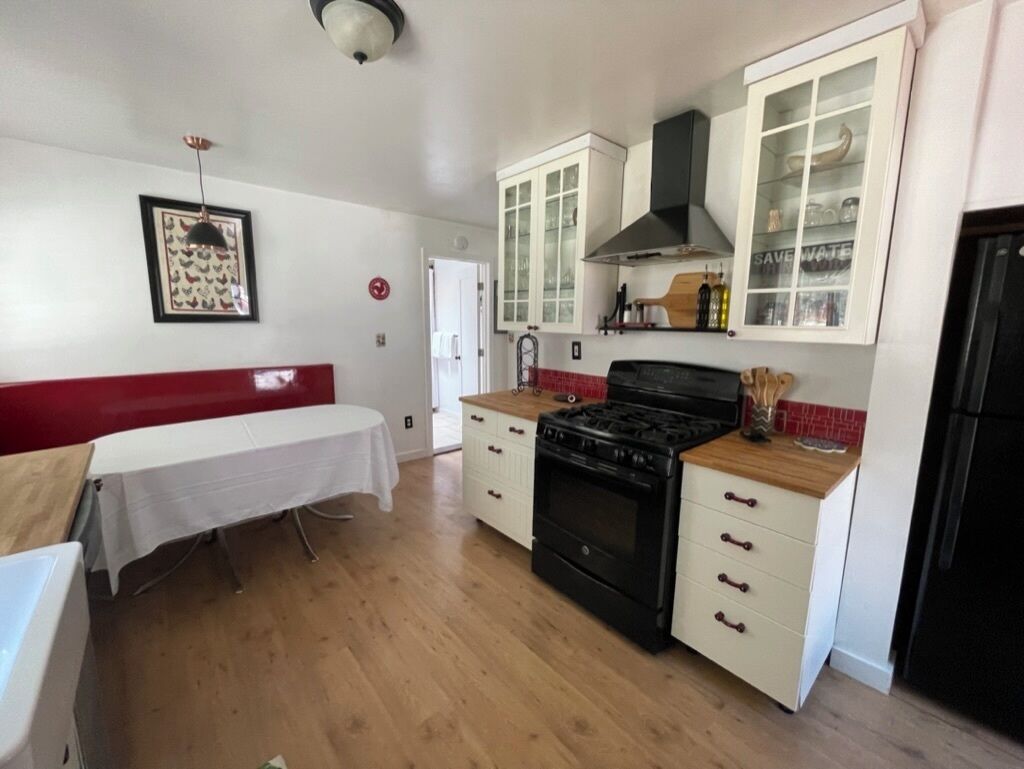 A kitchen with white cabinets, a black stove, and a wooden countertop.
