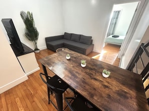 A dining area with a wooden table, two chairs, a grey sofa, and a potted plant.