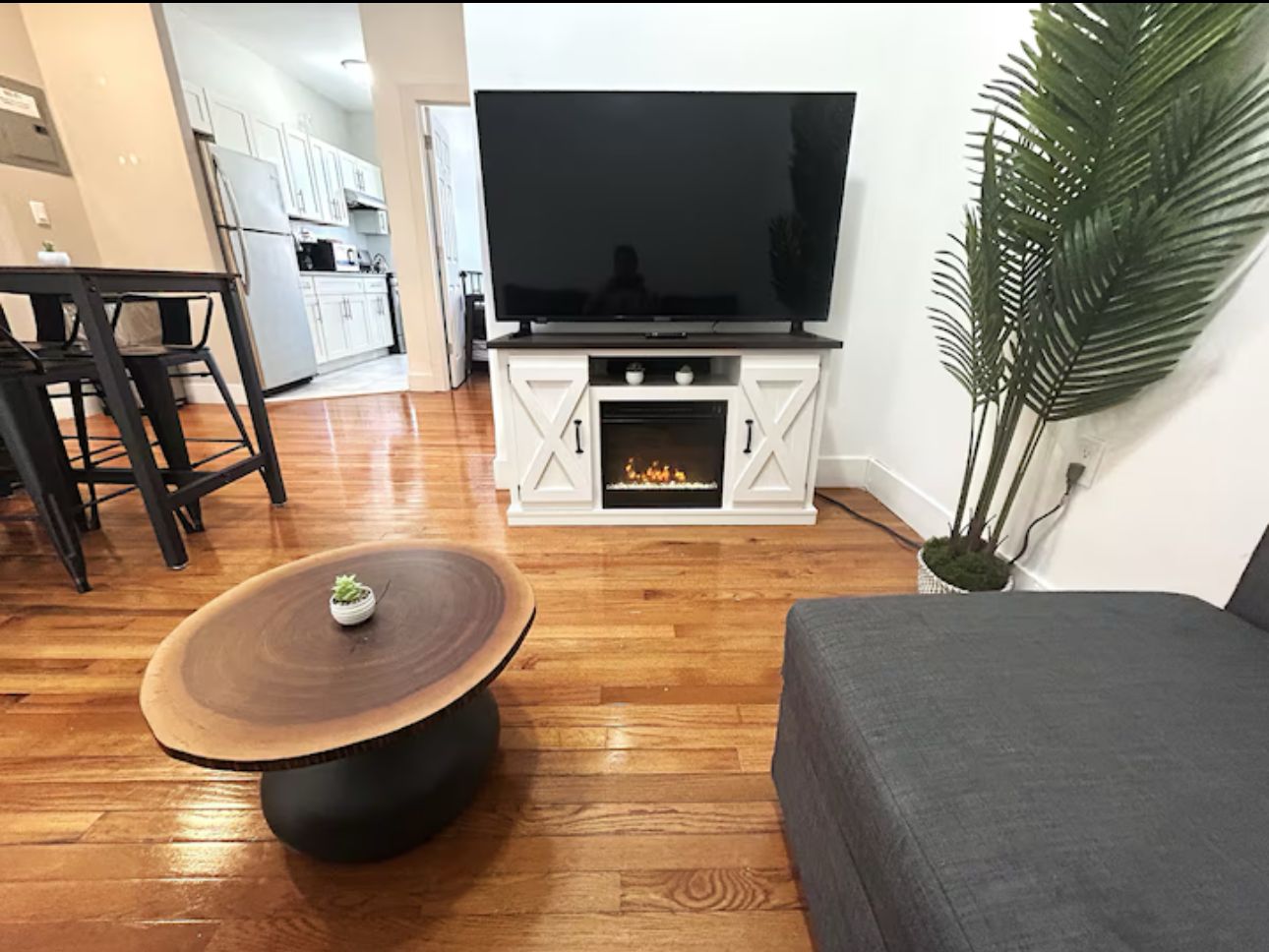 Un salón con una televisión de pantalla plana, una mesa redonda de centro, un sofá gris y una planta en maceta.