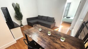 A dining area with a wooden table, two chairs, a grey sofa, and a potted plant. - Charming 2-bedroom apartment in lovely Brooklyn, 20mins to Manhattan (Brooklyn)