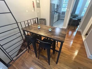 A dining area with a wooden table and four chairs, a fire extinguisher on the wall, and a view of the kitchen and living area through an open door.