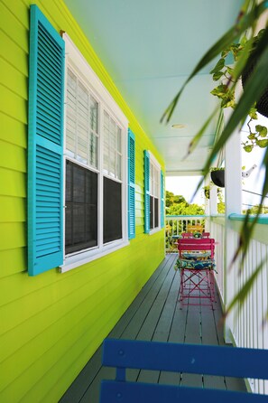 A bright green porch with blue shutters, a wooden bench, and a small table with chairs.