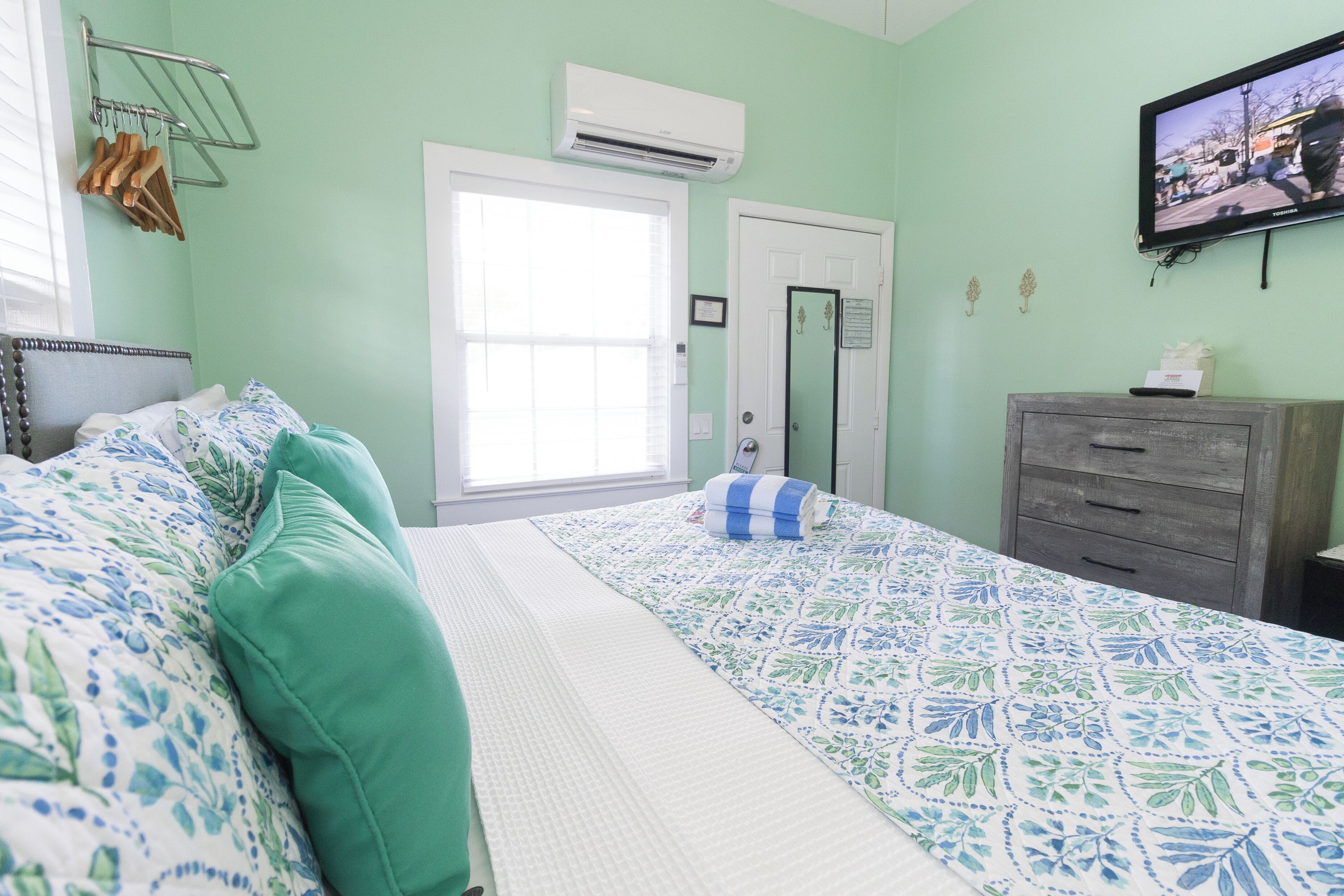 Une chambre à coucher avec un lit, une commode, un climatiseur et un téléviseur fixé au mur.