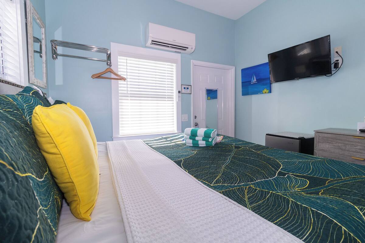 A bedroom with a bed, a TV mounted on the wall, and a door with a painting.
