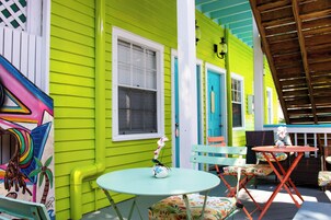 Un'area esterna vivace con sedute colorate e un piccolo tavolo, circondata da un edificio verde brillante con rifiniture bianche.