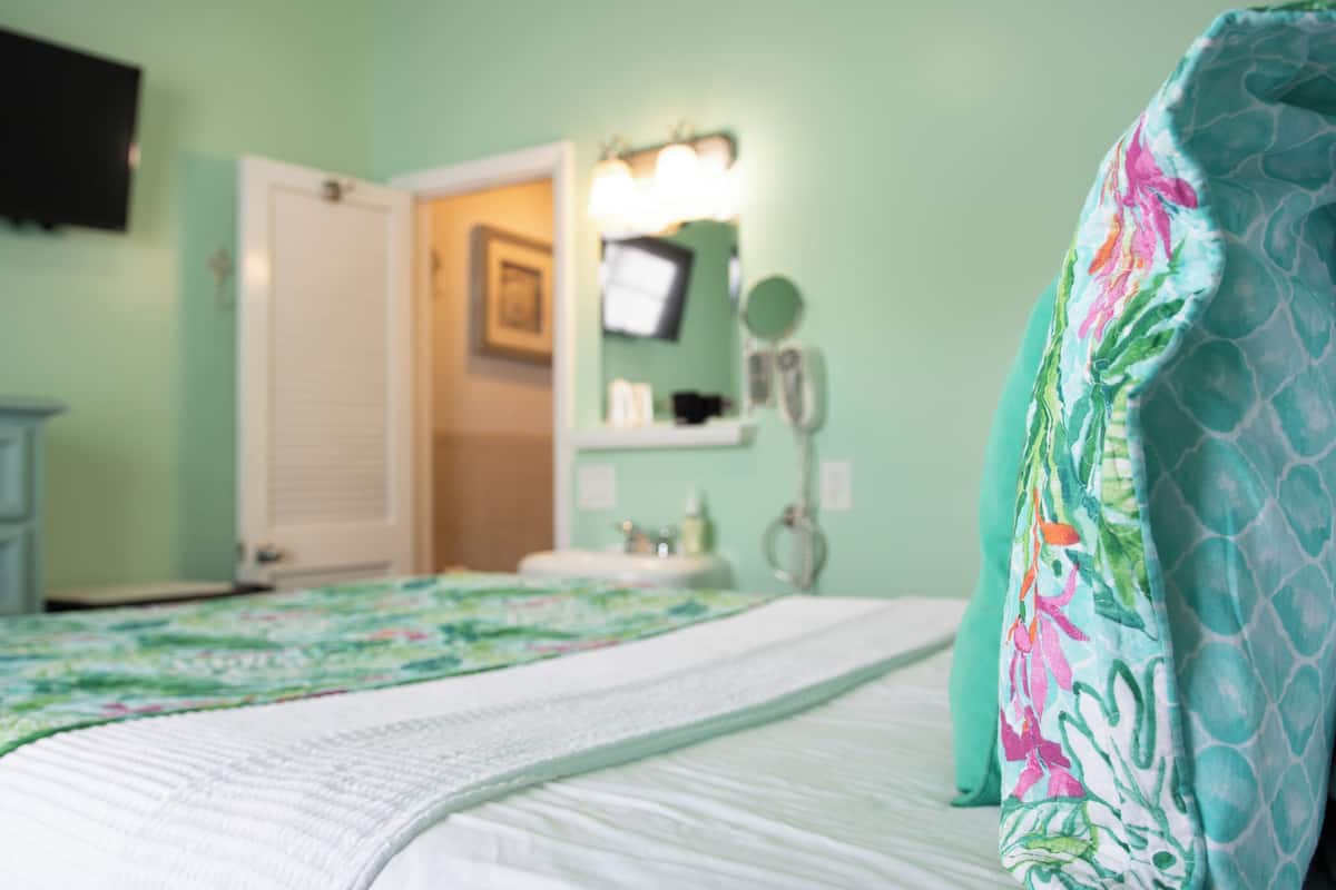 A bedroom with a bed, a nightstand, a dresser, a mirror, and a bathroom visible through an open door.