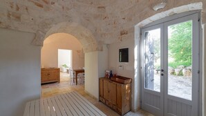 Une pièce aux murs de pierre, avec un banc en bois, une armoire en bois et une porte donnant sur l’extérieur.