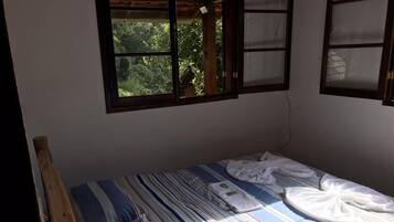 A single bed with striped bedding, a wooden headboard, and two windows with frosted glass panes.