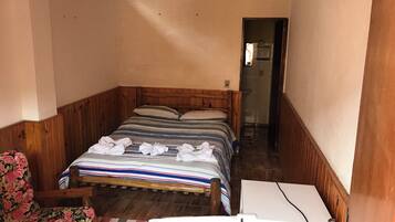 Um quarto pequeno e acolhedor, com cama de madeira, uma poltrona com estofamento floral e um refrigerador branco.