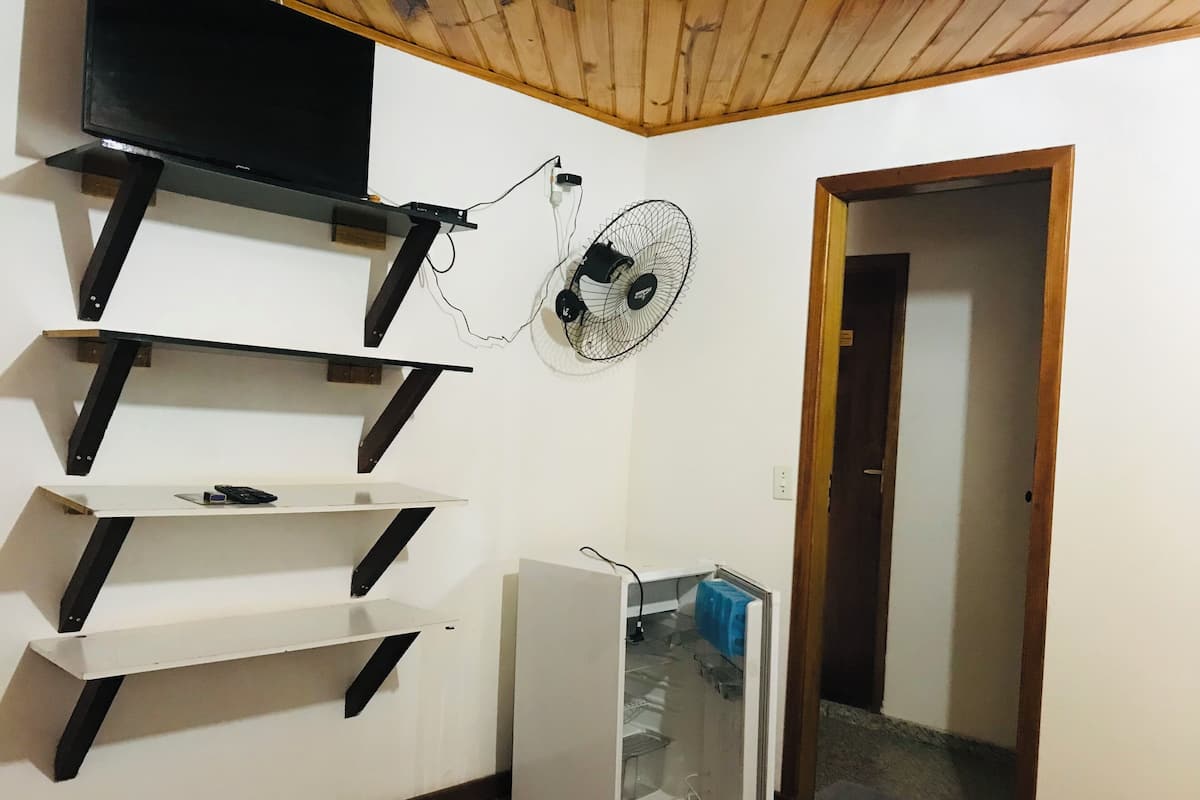 A room with a TV mounted on a wooden beam, a wall-mounted fan, and a white refrigerator.