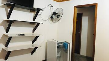 A room with a TV mounted on a wooden beam, a wall-mounted fan, and a white refrigerator.