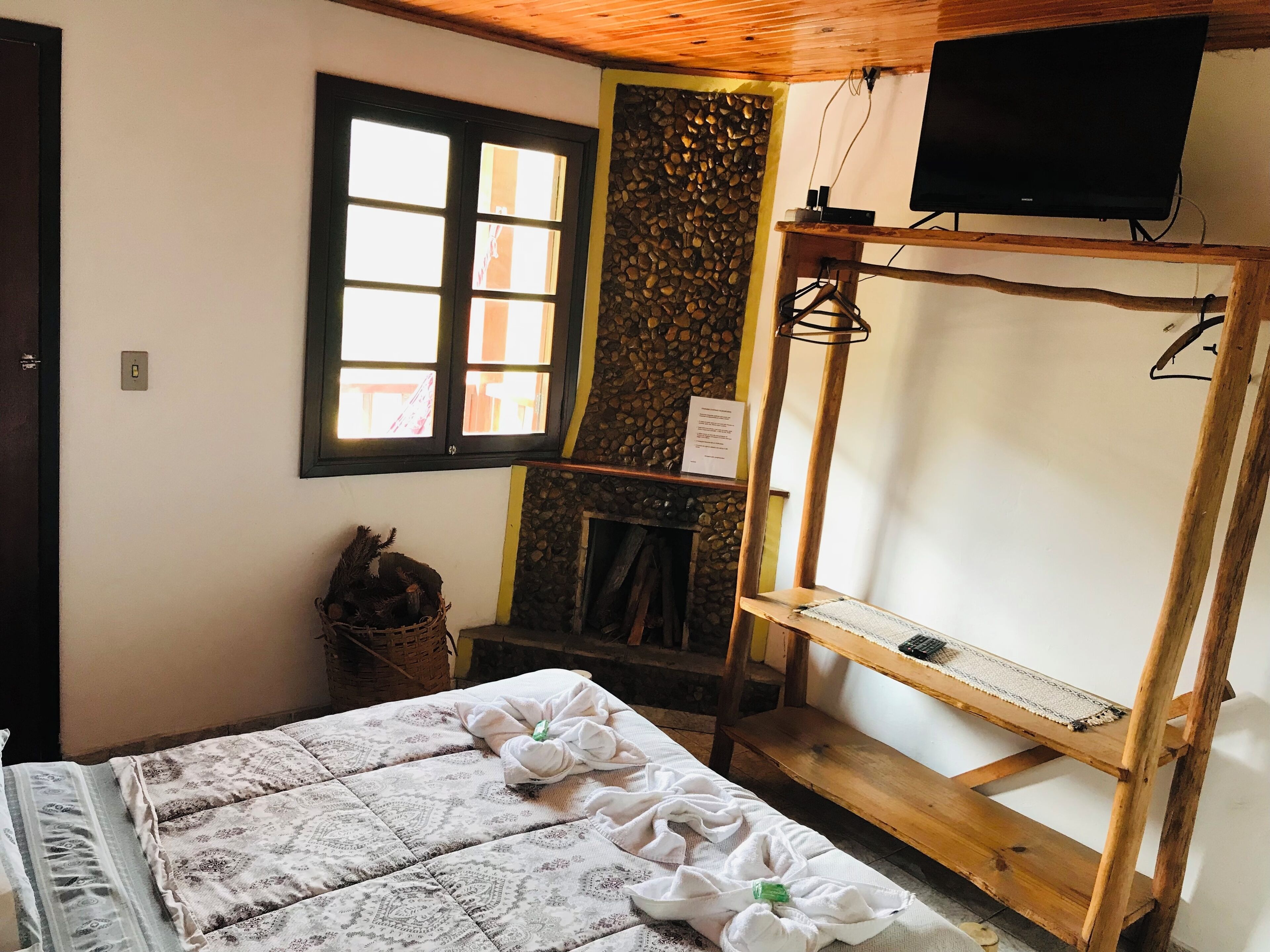 Una habitación con una cama, un estante de madera, un televisor y una ventana con vistas a edificios.