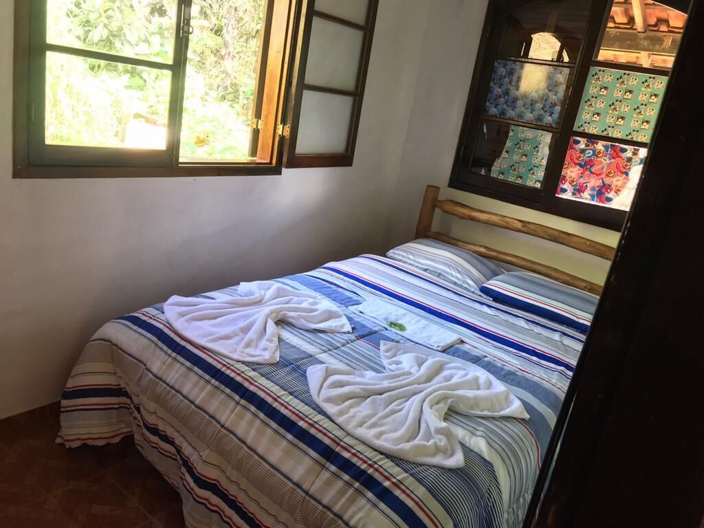 Un dormitori amb un llit, roba de llit a ratlles, una finestra amb vista a vegetació i una paret amb un panell decoratiu.