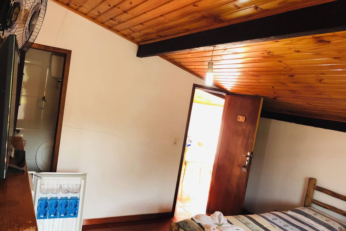 A room with a wooden ceiling, a bed with a striped bedspread, a wooden door, and a white cabinet with blue handles.