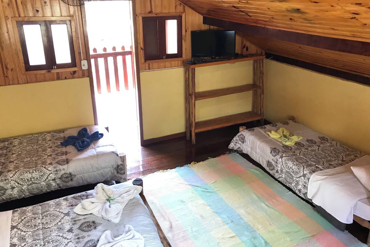 A cozy attic room with wooden walls, a sloped ceiling, two single beds, a TV on a wooden stand, and a fan on the ceiling.