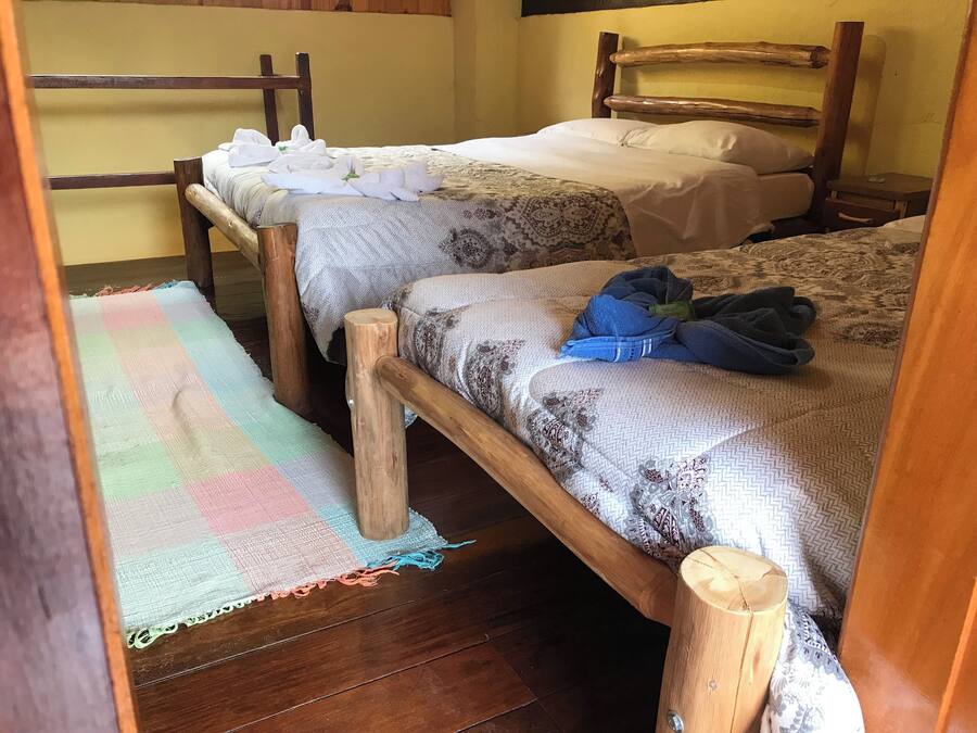 Una habitación con dos camas de madera, cada una con una colcha y almohadas estampadas. Hay un tapete de cuadros de colores en el suelo.