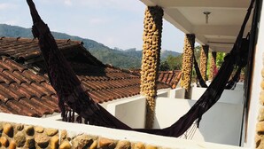 A stone wall with a hammock, a tiled roof, and a view of hills. - Pousada Cantinho da Montanha (Itatiaia)