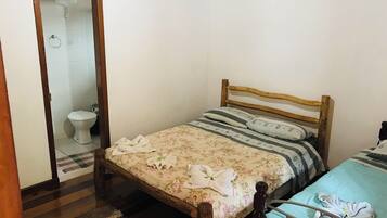 A bedroom with a wooden bed, a small bedside table, a single bed with a floral bedspread, a blue bedspread, and a white toilet.