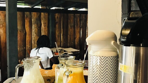A rustic wooden table with various food items and containers, including a pitcher of milk, a jar of jam, and a thermos. - Pousada Cantinho da Montanha (Itatiaia)