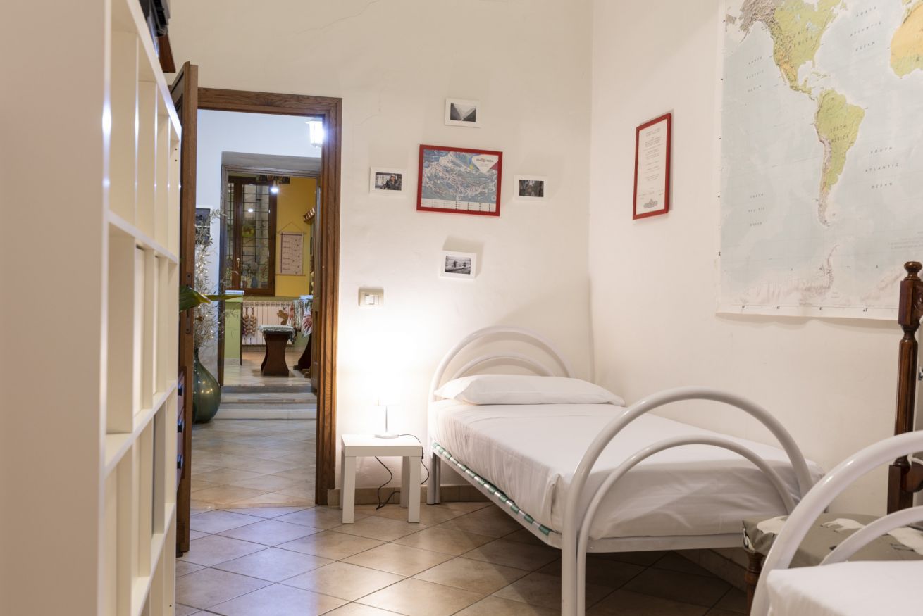 A bedroom with two single beds, a small bedside table, a wall-mounted map, and a door leading to another room.
