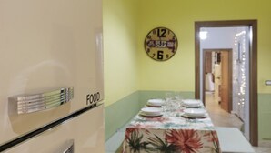 A dining area with a table set for four, a clock on the wall, and a door leading to another room.