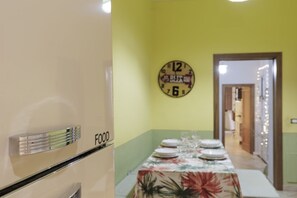 Un comedor con una mesa dispuesta para cuatro personas, un reloj en la pared y una puerta que da a otra habitación.