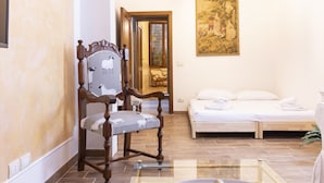Una habitación con una silla de madera, una cama, una mesa de vidrio y un cuadro en la pared.