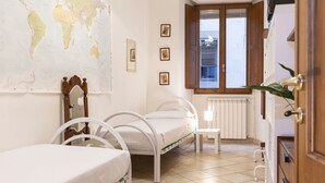 A bedroom with two beds, a world map on the wall, a window with a view, and a radiator.