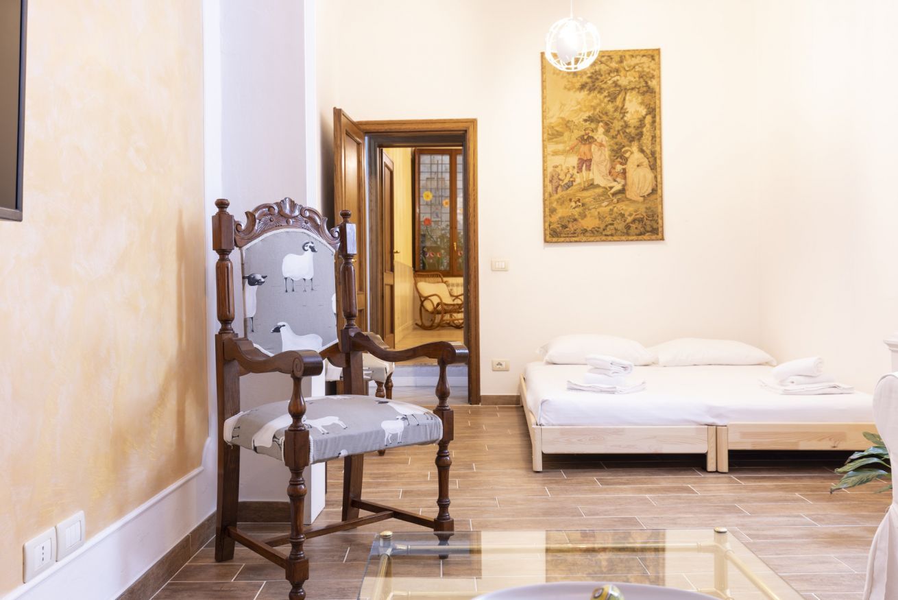 Une pièce comprenant une chaise en bois, un lit, une table en verre et un tableau accroché au mur.