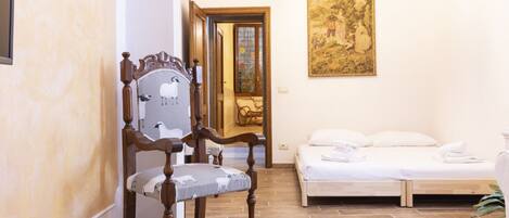 A room with a wooden chair, a bed, a glass table, and a painting on the wall.