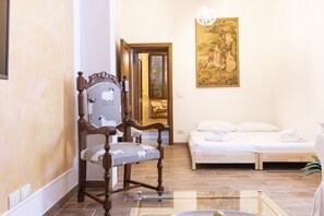 A room with a wooden chair, a bed, a glass table, and a painting on the wall.