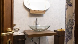 A bathroom with a wooden vanity, a glass bowl sink, and a hanging mirror.