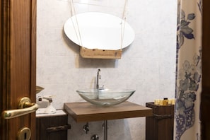 Un baño con tocador de madera, lavabo de vidrio y espejo colgado.