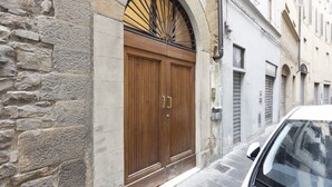 Un edificio de piedra con una puerta doble de madera, un toldo metálico y un coche blanco estacionado frente a él.