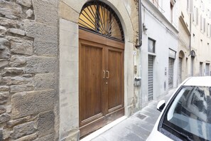 A stone building with a wooden double door, a metal awning, and a white car parked in front. - San Niccolò Elegant Apartment (Firenze)