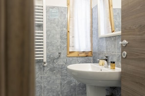 A bathroom with a white sink, a wooden-framed mirror, and grey marble tiles.