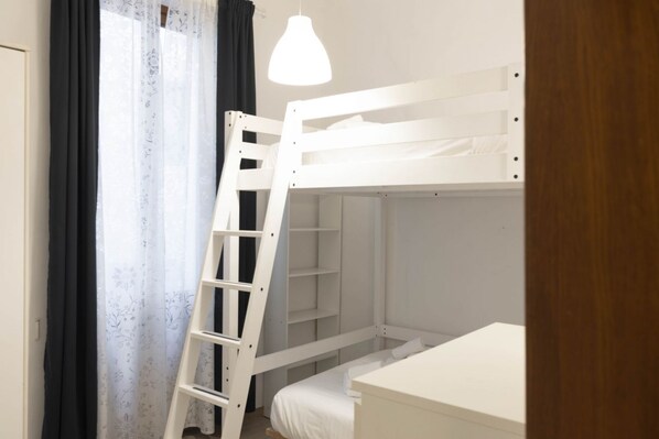 A bunk bed with a ladder, a bedside table, and a hanging light fixture.