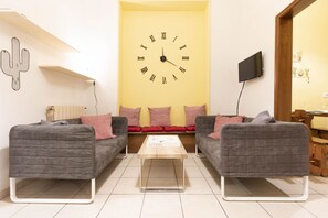 A living room with two grey sofas, a wooden coffee table, a large wall clock, and a cactus decoration.