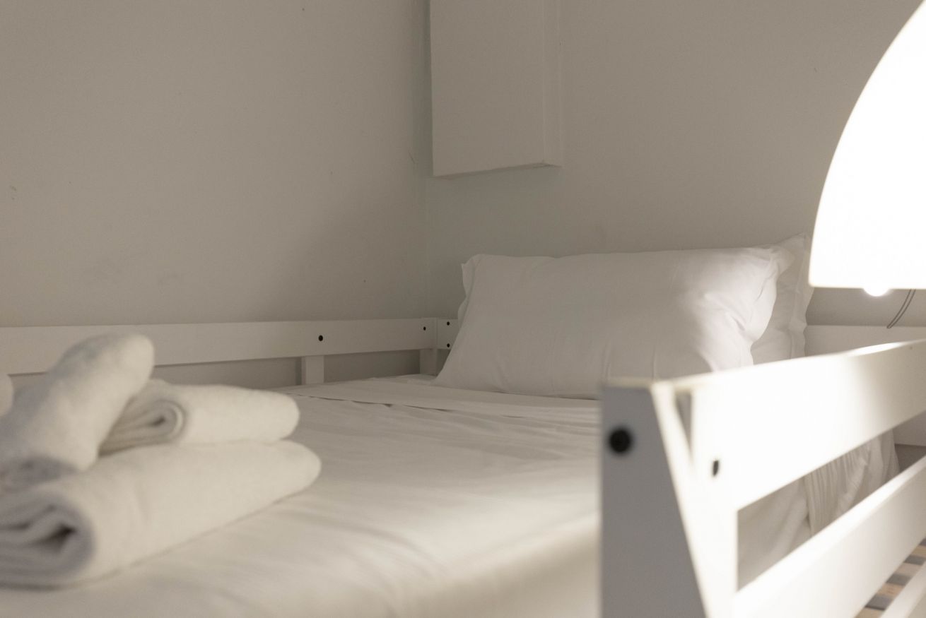 Un lit simple, blanc, avec une tête de lit, un oreiller et des serviettes enroulées posées sur le lit.