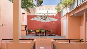 Un cortile con tavolo e sedie, un ombrellone grande e una scala che conduce a un piano superiore.