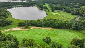 A golf course with a large lake, surrounded by dense forest.