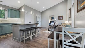 A modern kitchen with bar stools, a dining area with a table and chairs, and a living room with a sofa and a coffee table.