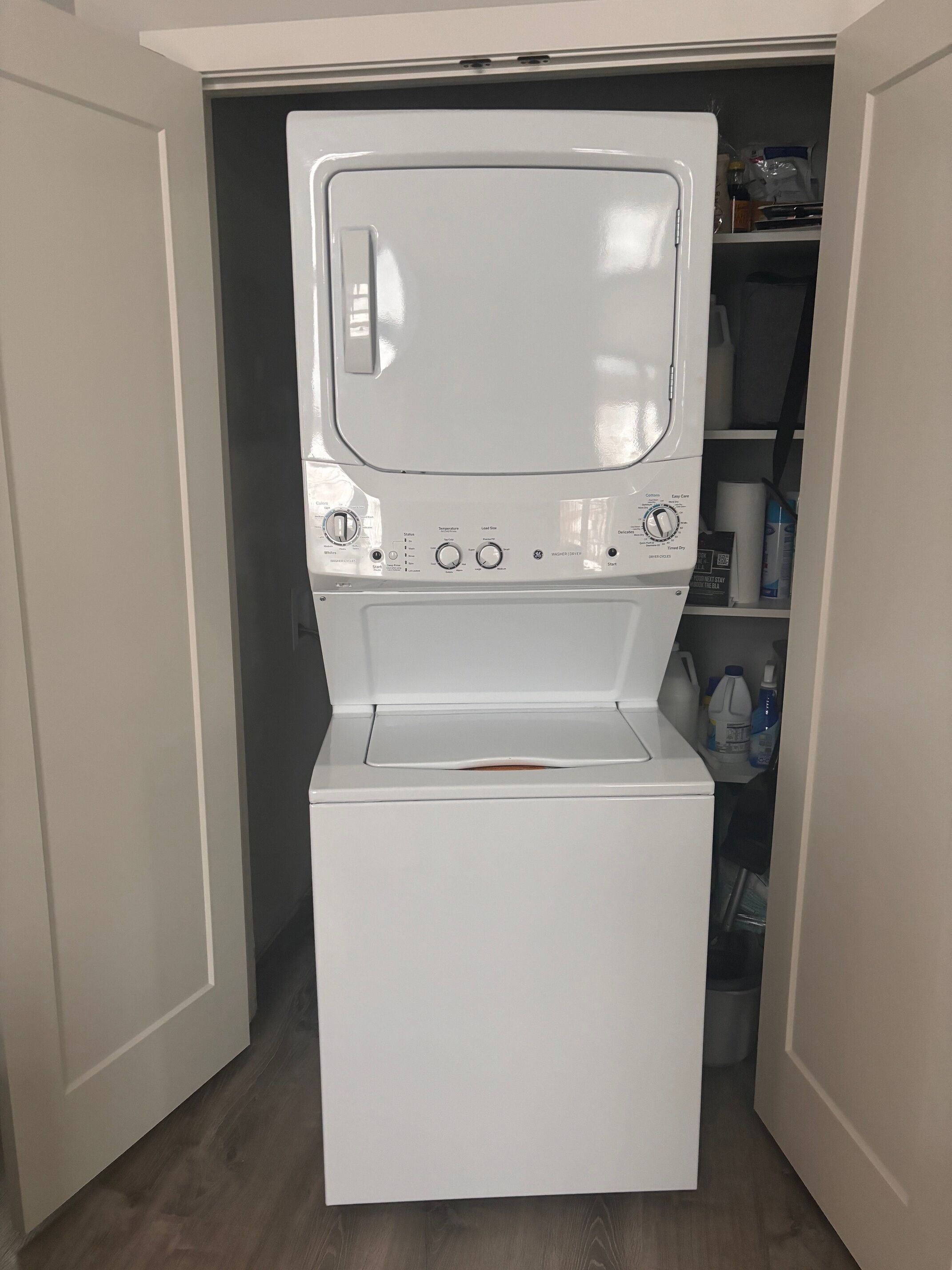Un appareil compact, blanc, combinant lave-linge et sèche-linge, installé dans une petite buanderie avec un plancher en bois.
