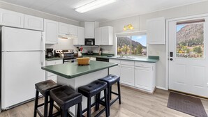 Une cuisine moderne avec des meubles blancs, un îlot central vert doté de tabourets, un four à micro-ondes et une vue sur un paysage montagneux par la fenêtre.