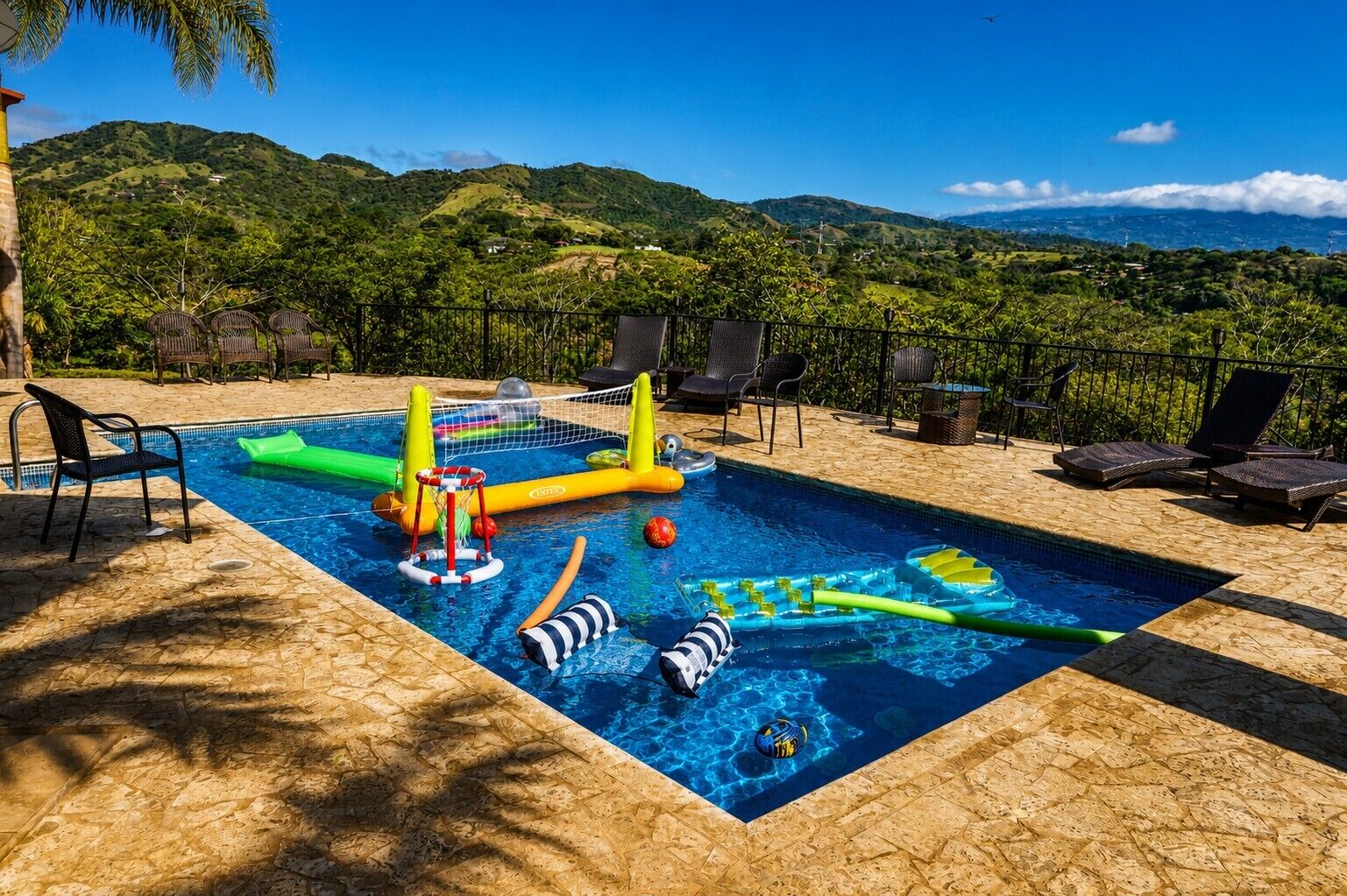 A swimming pool with inflatable toys, lounge chairs, and a view of green hills.