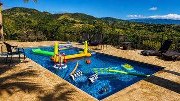 A swimming pool with inflatable toys, lounge chairs, and a view of green hills.