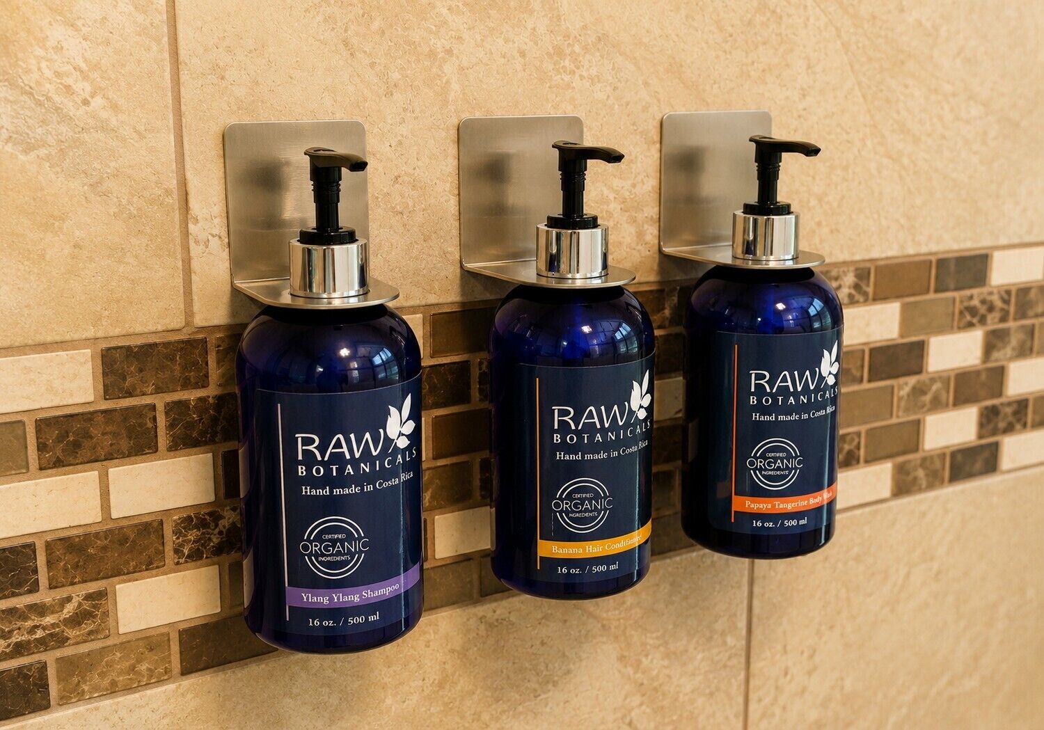 Tres botellas de champú Raw Botanicals sobre una pared con un diseño de mosaicos.