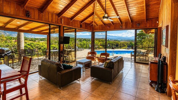 Un amplio espacio interior con techo de madera, un ventanal grande y una piscina visible a través del vidrio.