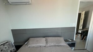 Una habitación de hotel con cama, mesita de noche, una silla y un equipo de aire acondicionado.